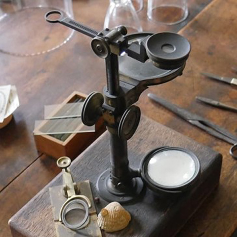 An old microscope placed on a wooden desk.