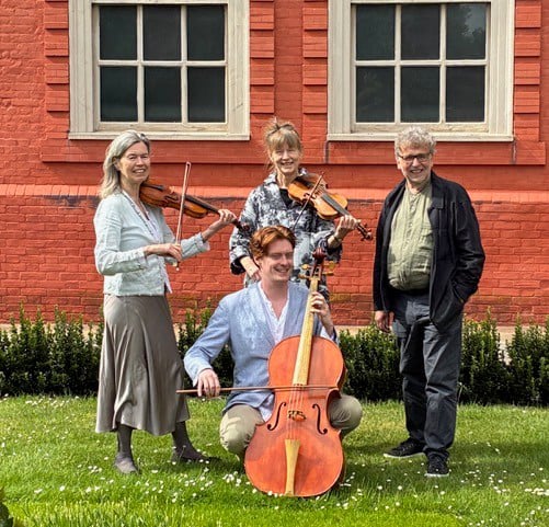 4 people smiling holding string instruments on a lawn.
