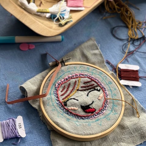 An embroidery hoop with needles and threads laid out next to it.