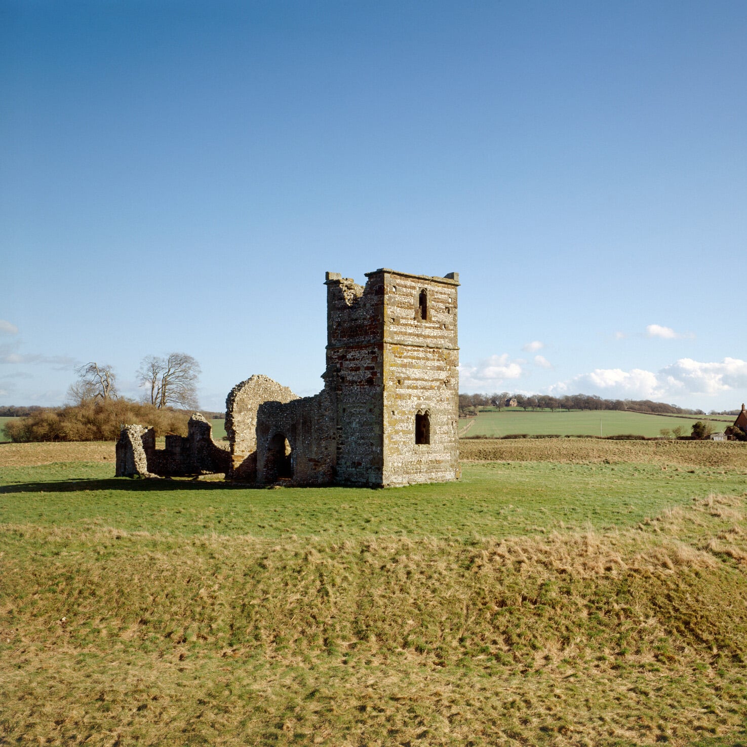A view of Knowlton Church underneath a bright blue sky, surrounded by fields.