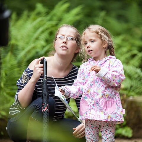 A young girl wearing a waterproof coat holds a sheet of paper and a woman kneels beside her in the gardens at Belsay Hall.