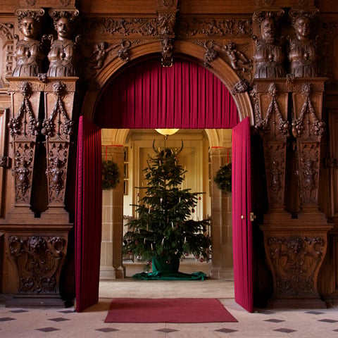An interior room at Audley End House with oak panelling and a decorated Christmas tree is stood in the doorway. 