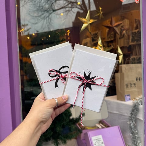 Someone holding up two paper Lino printed Christmas cards in front of a shop window.