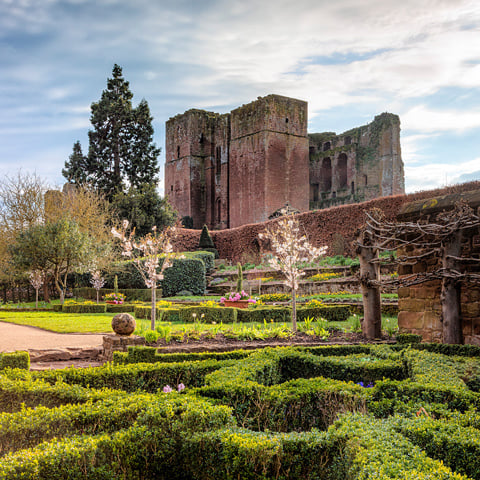 A view of Kenilworth Castle ruins with the Elizabethan garden in the foreground on a sunny day.