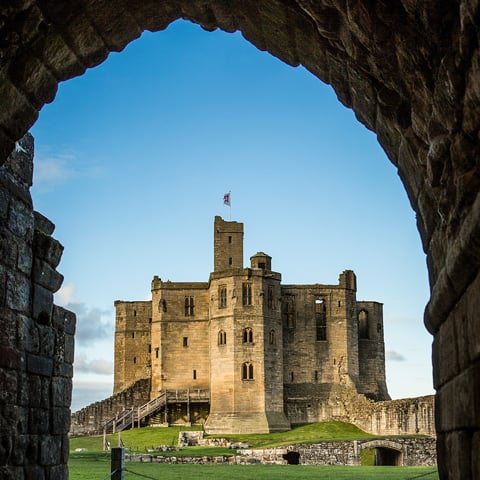 A photo of Warkworth Castle through a stone archway on a winters day.