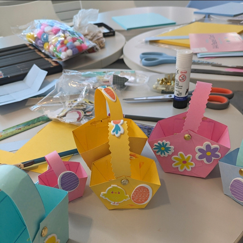 A variety of colourful Easter themed baskets laid out on a table with craft supplies in the background.