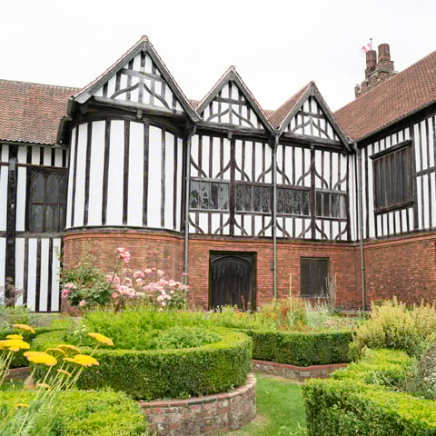 A view of the courtyard gardens and blooming flowerbeds with the black and white timber-framed Gainsborough Old Hall in the background.