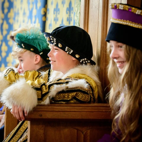 Three children dressed in Tudor costumes smile at Gainsborough Old Hall.
