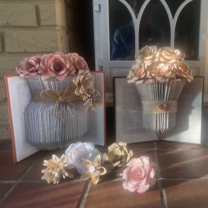 Two handmade book vases with colourful pink flowers displayed in them.