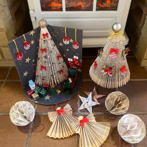 Several folded book Christmas decorations displayed on the floor next to a woodburner.