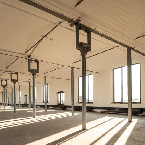 A view of an interior open space with large supporting metal beams and large windows at Shrewsbury Flaxmill Maltings..