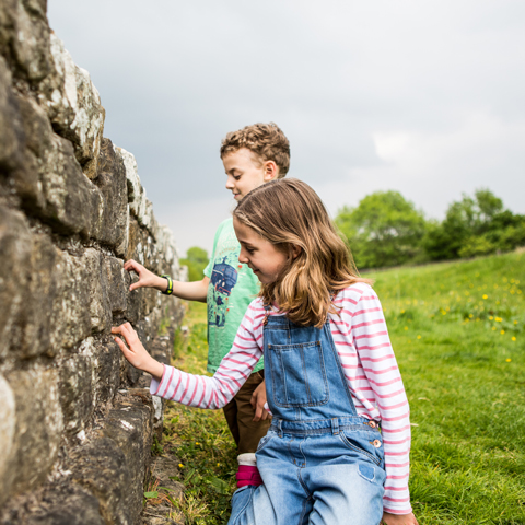 Two young children touch the Roman stone wall at Housesteads Roman Fort.