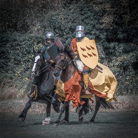 Two re-enactors dressed as knights ride two horses