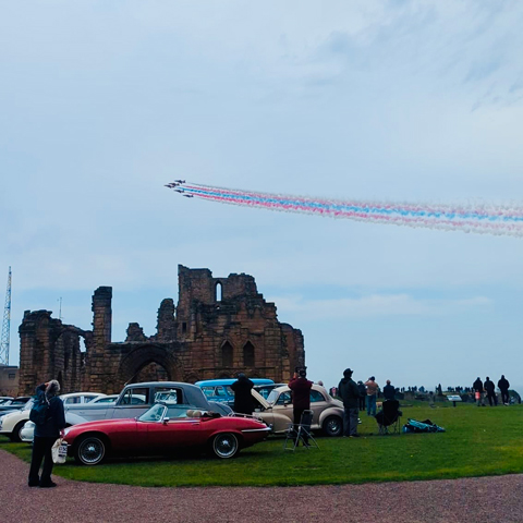 An air display over Tynemouth Priory with classic cars parked on the lawn.