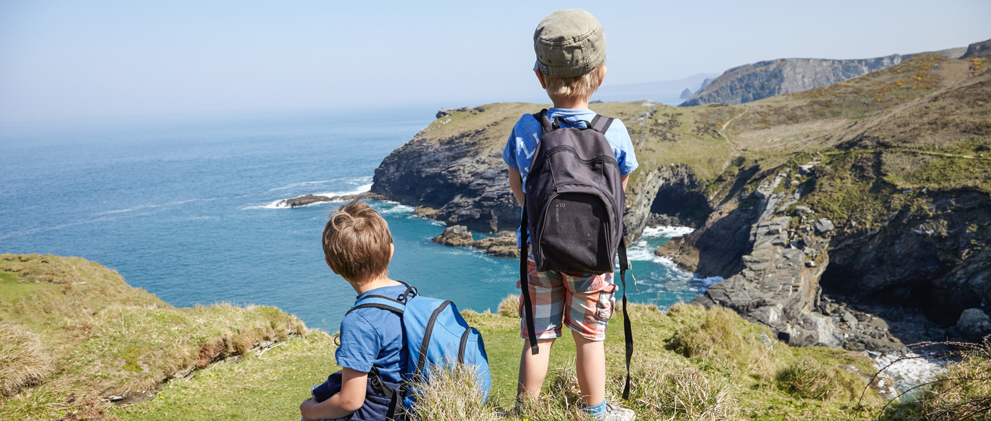Two young boys look at the view at Tintagel Castle on a sunny day.