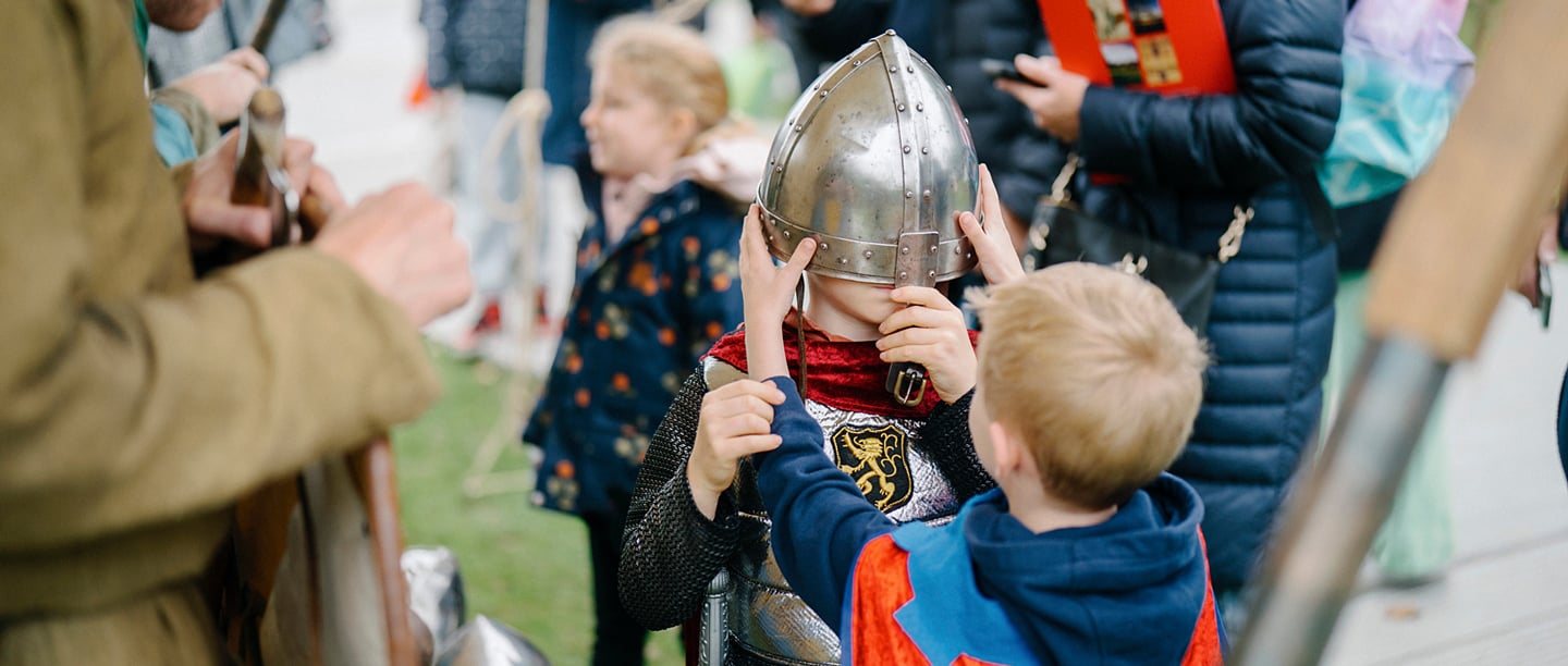 Two young children help each other dress up in medieval knight's armour at the Battle of Hastings Weekend event.