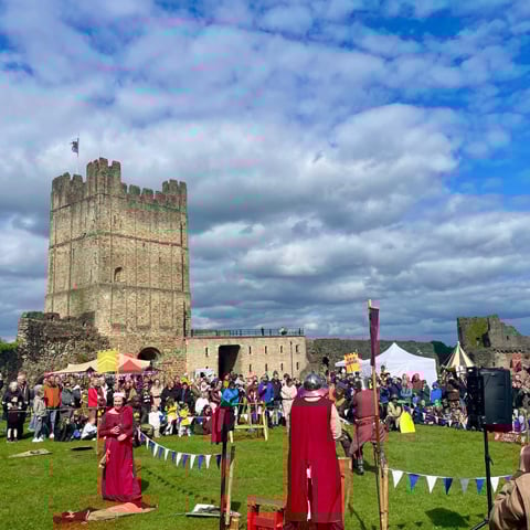 A fair with groups of people gathered in the grounds of Richmond Castle on a sunny day.