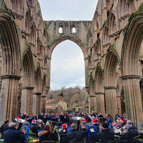 A brass band play to an audience in the middle of the ruins at Rievaulx Abbey.