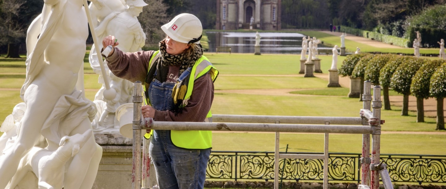 Photo of someone in a hi-vis jacket and safety helmet repainting a statue at Wrest Park in Bedfordshire whilst standing on scaffolding